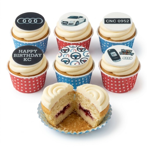 Six vanilla cupcakes with cream frosting, decorated with Audi car theme toppers, including logo, car, key, and steering wheel patterns.