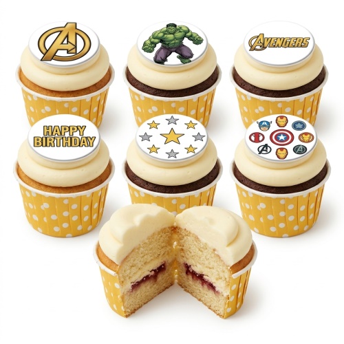 A selection of Avengers themed birthday cupcakes with white frosting and yellow polka dot wrappers, featuring Hulk, Avengers logo, and superhero symbol toppers, with one cupcake cut open revealing jam filling.