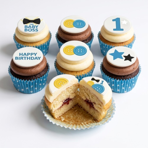 Baby Boss themed 1st birthday cupcakes for boys with blue and yellow buttons, stars, and bow tie toppers on vanilla and chocolate frosting in blue polka dot cases.