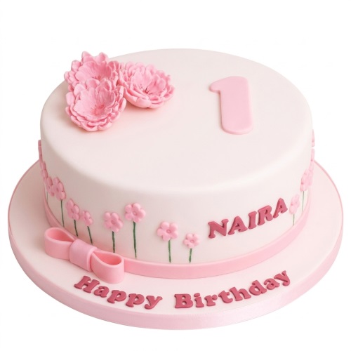 Round white and pink birthday cake with pink fondant flowers, a pink number one topper, and a pink bow.