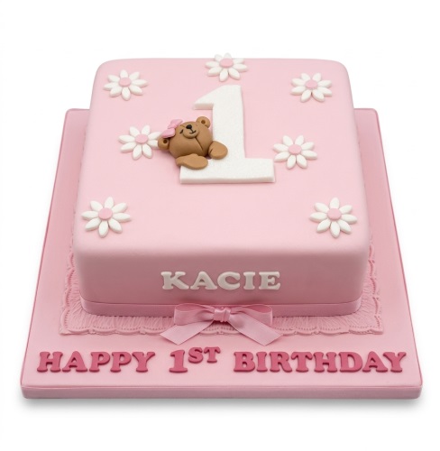 Pink square 1st birthday cake with white number one, teddy bear, and daisy flowers.