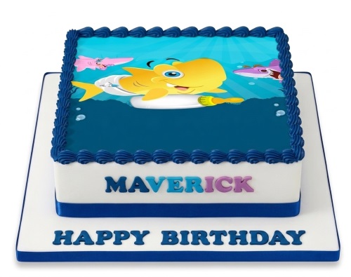 Square white birthday cake with blue ribbon and edible image of a yellow baby shark character in an underwater scene with blue piped borders.