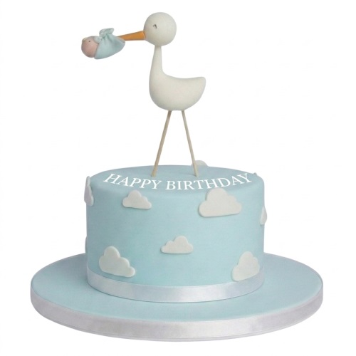 Light blue single-tier cake with a stork topper carrying a baby, white clouds, and a white ribbon.