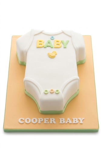 White baby grow shaped cake with green trim, yellow and green 'BABY' text, a yellow duck, and pastel buttons on an orange board.
