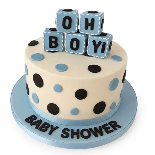 Round cream baby shower cake with blue and black polka dots, topped with blue "OH BOY!" blocks and a "BABY SHOWER" message on the board.