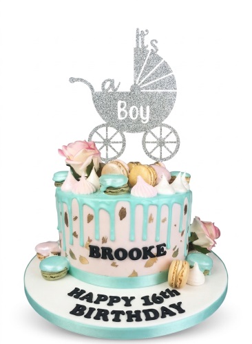 Round pastel pink cake with mint green drip, gold accents, macarons, pink roses, and a silver glitter 'It's a Boy' baby pram topper.