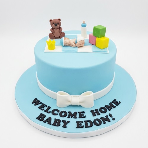 Light blue baby shower cake with sleeping baby, teddy bear, blocks, and personalised message board.
