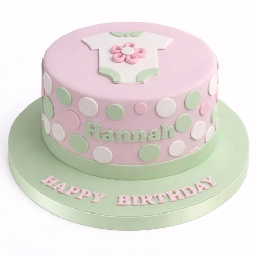 Round pink and mint green baby girl birthday cake with white polka dots and a baby grow decoration.