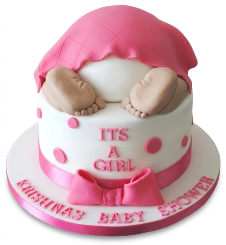 White round baby shower cake with pink blanket, baby feet, pink polka dots, pink bow, and 'It's a Girl' message. Personalised name on cake board.
