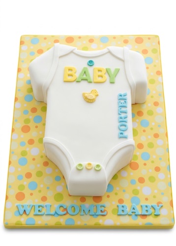 White baby grow cake with yellow and green 'BABY' text, a yellow duck, and a polka dot board with 'WELCOME BABY' text.
