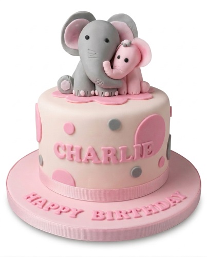 Round pink and white birthday cake with grey and pink fondant elephants and polka dots.