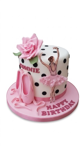 White single-tier cake with black polka dots, pink sugar rose, pink ballet shoes, and a ballerina figure on a pink cake board.