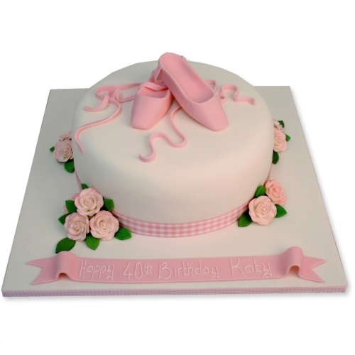 Round white cake with pink ballet pointe shoes, ribbons, and sugar roses.