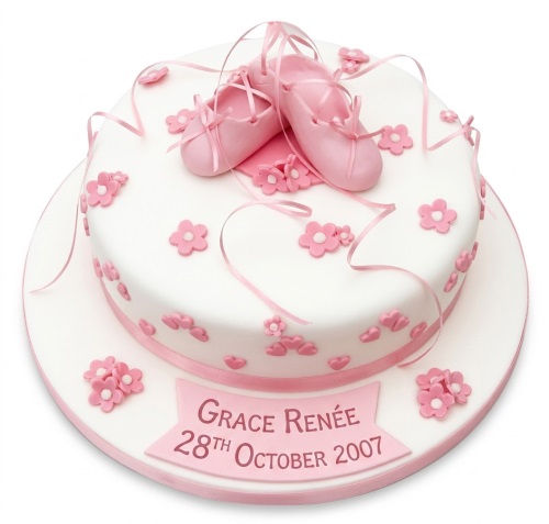 White round cake with pink ballet shoes, ribbons, and small pink flowers