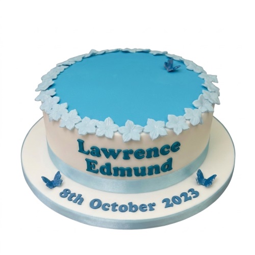 Round white and blue cake with light blue flowers and blue butterflies, featuring a personalised message.