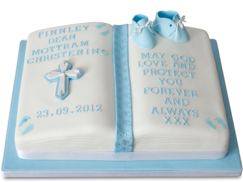 White open book christening cake with blue baby booties, a cross, and custom text.
