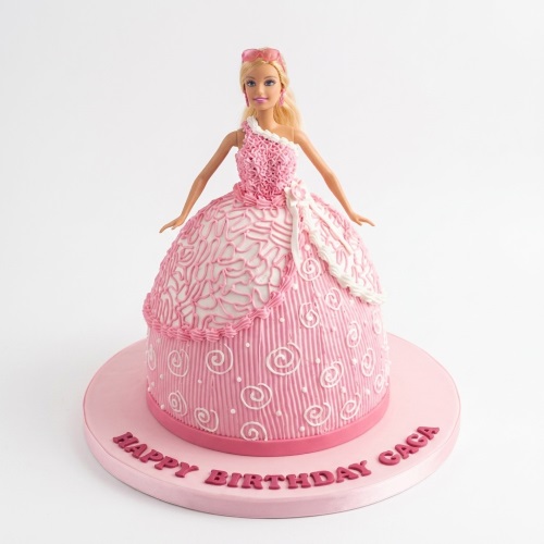 Pink and white Barbie doll birthday cake with decorative icing on a pink cake board.