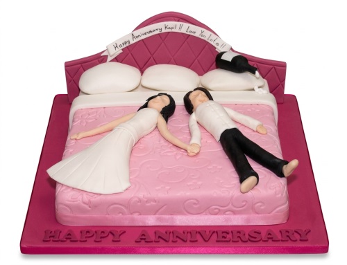 Anniversary cake featuring a couple on a pink bed with a headboard and a personalised banner.