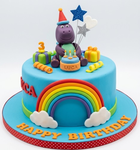 Blue fondant birthday cake with a purple dinosaur, rainbow, stars, gift boxes, and a custom age topper.