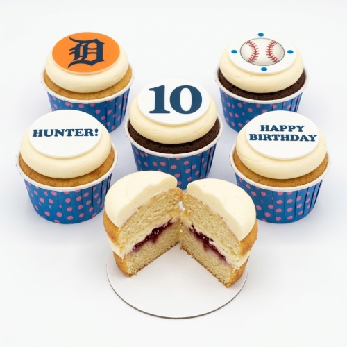 Vanilla and chocolate cupcakes with baseball, team logo, custom age, and personalised name toppers in blue polka dot cases.