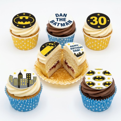 Batman themed birthday cupcakes with bat signal, cityscape, and cape toppers, in yellow and blue cases.