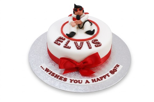 White round birthday cake with an Elvis Presley figure, red ribbon, and "ELVIS" lettering.