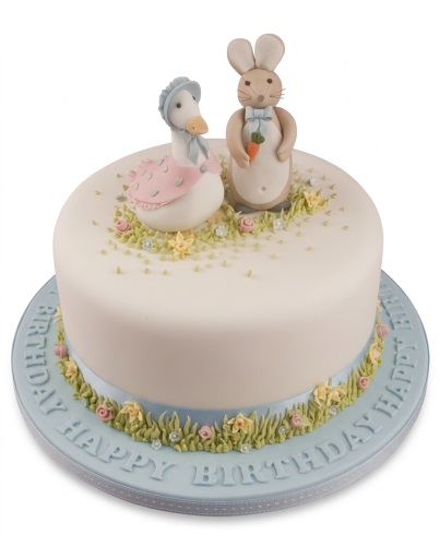 Round white Peter Rabbit birthday cake with Peter Rabbit and Jemima Puddle-Duck figurines, green grass, and pastel flowers.