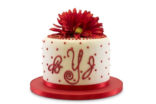 Single-tier white birthday cake with red polka dots and a large red dahlia flower on top, with a custom message.