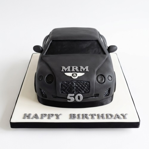 Black 3D luxury car birthday cake on a white board with a custom age and 'Happy Birthday' message.