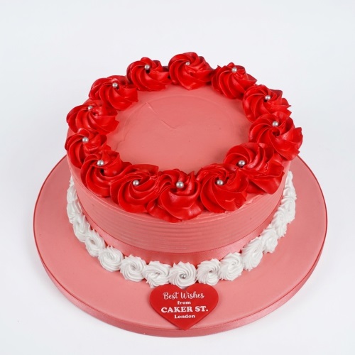 Round pink birthday cake with red buttercream roses, white piping, and silver pearls.