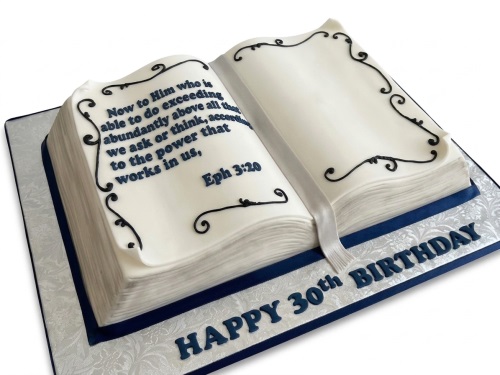 White open book cake with dark blue text and scroll details, white ribbon bookmark, on a patterned board.