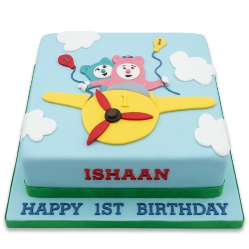 Light blue fondant cake with a yellow airplane, two cartoon characters, white clouds, and red and yellow number '1' balloons, with 'ISHAN HAPPY 1ST BIRTHDAY' message.