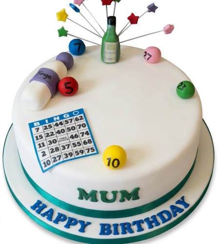 Round white birthday cake with bingo card, numbered balls, champagne bottle, and star toppers.