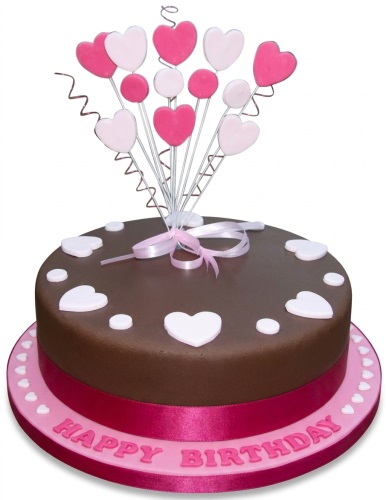 Round chocolate-coloured birthday cake with pink and white heart decorations and a "Happy Birthday" message.