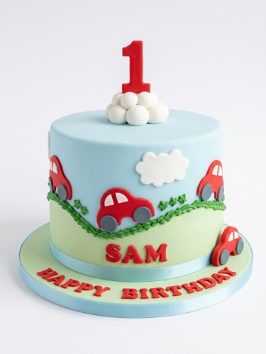 Light blue and green single-tier cake with red car decorations, white clouds, and a red number one topper.