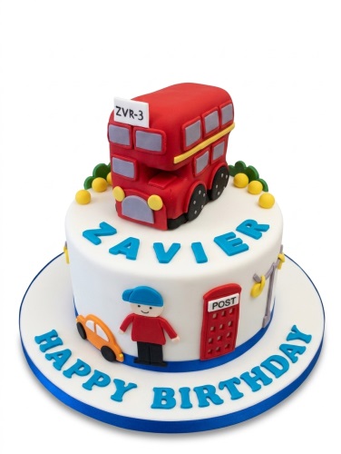 Two-tier white birthday cake with a red London bus, a boy character, orange car, and red post box.