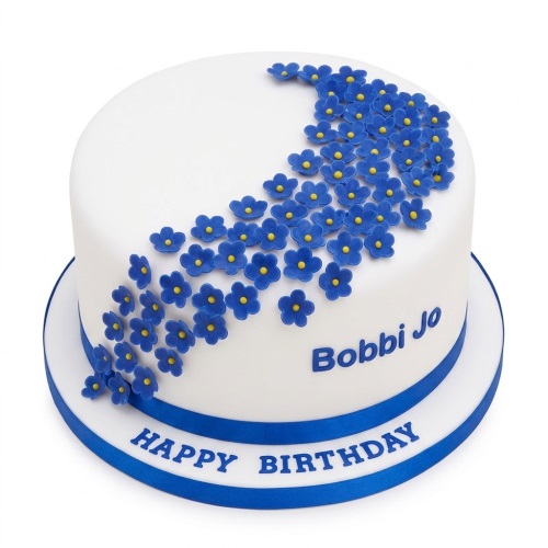 Round white birthday cake decorated with blue sugar flowers and a blue ribbon, with space for a personalised message.