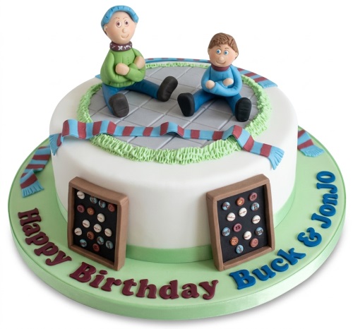 Round white birthday cake with two male figures, a claret and blue scarf, and badge displays.