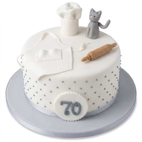 White round baking theme birthday cake with chef's hat, apron, rolling pin, grey cat, and custom age topper.