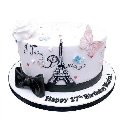 White round birthday cake with black Eiffel Tower, pink and blue butterflies, a white rose, and a black bow, with a custom age message.