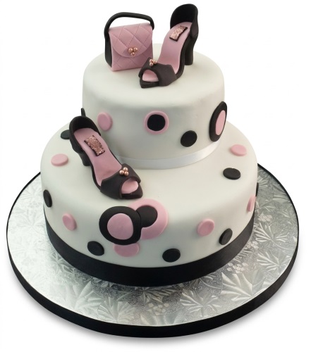 Two-tiered white birthday cake decorated with black high heels, a pink handbag, and pink and black polka dots.
