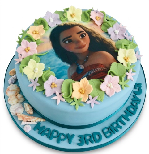 Two-tier Moana birthday cake with edible image, pastel sugar flowers, and seashells.
