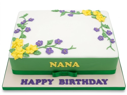 Rectangular white and green cake with yellow and purple sugar flowers, green ribbon, and custom message.