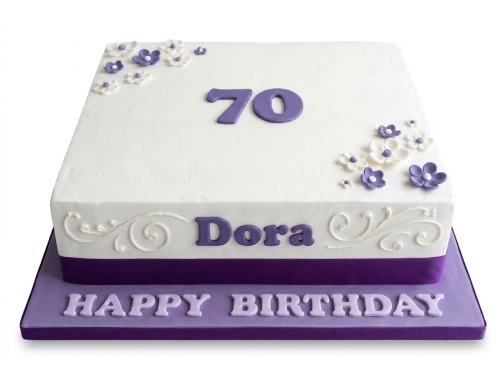 Square white birthday cake with purple base, white and purple fondant flowers, white swirls, and custom age topper.