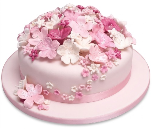 Round pink birthday cake decorated with a cascade of pink and white edible flowers and a pink ribbon.