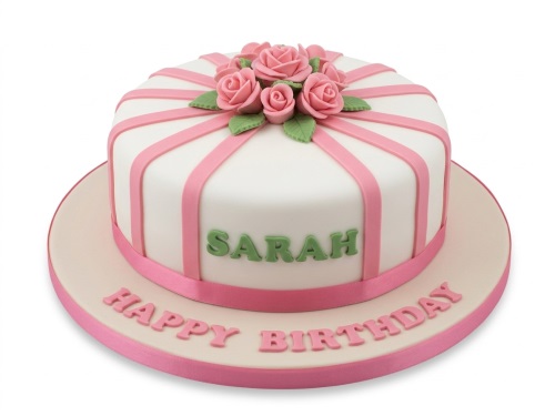 White round cake with pink sugar roses, green leaves, and pink ribbons, resembling a gift box, on a beige cake board.