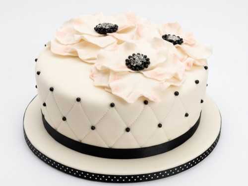 Elegant cream birthday cake with blush pink sugar flowers, black beaded centres, and a quilted side with black pearls.