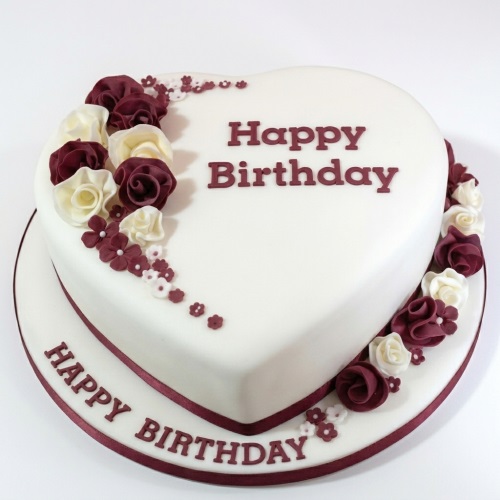Heart-shaped white birthday cake with maroon and cream fondant roses, small flowers, and a 'Happy Birthday' message.
