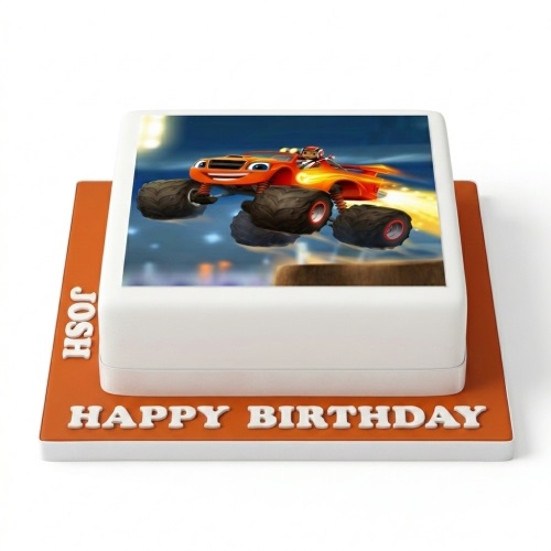 Square white cake with an edible image of Blaze the Monster Machine jumping, on an orange board with "Happy Birthday" text.