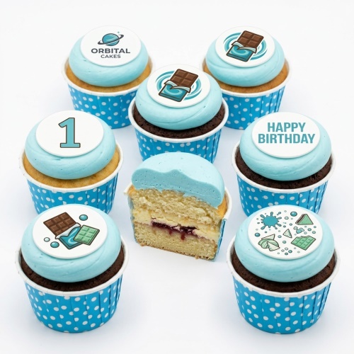 Set of light blue frosted cupcakes with white and blue polka dot wrappers, featuring edible chocolate bar and custom age '1' toppers, and a 'Happy Birthday' message topper.